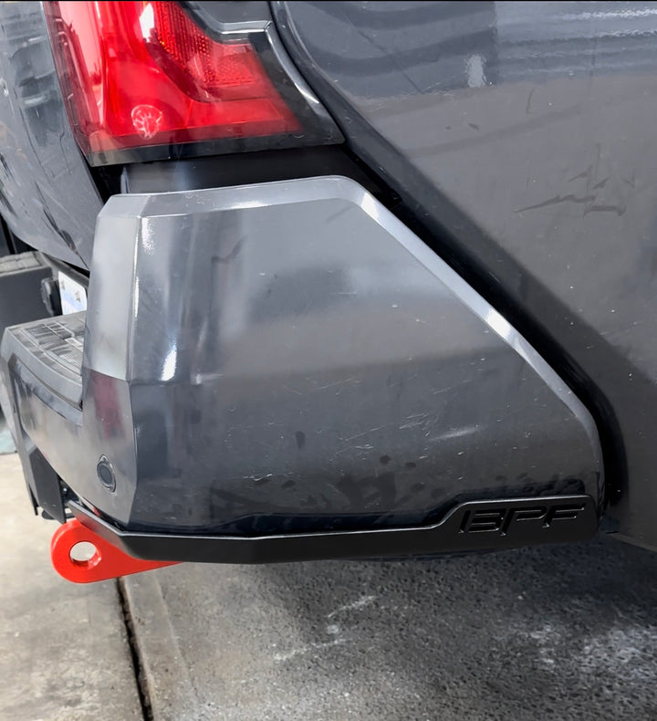 Close-up of a gray truck rear corner featuring BPF 4th gen Tacoma rear tow hooks with integrated skid plates in black with a red recovery hook attached, showcasing durable and functional truck accessories.