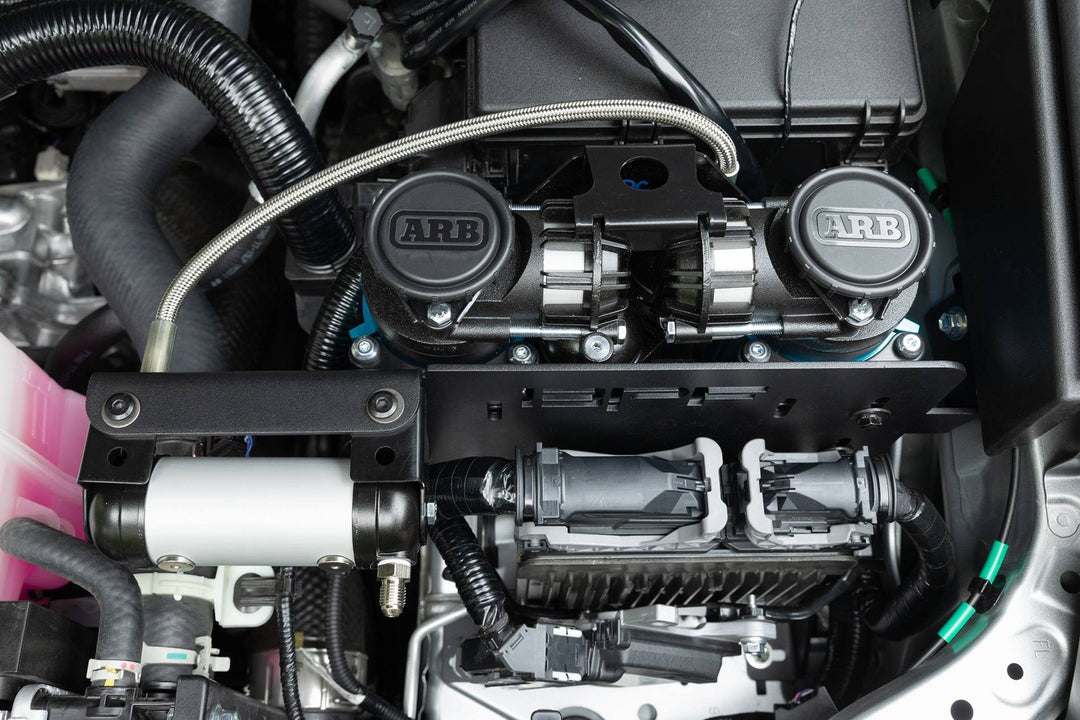 BPF 2025+ 4runner twin compressor mount installed in engine bay, showing dual ARB compressors secured on a black metal bracket with surrounding vehicle components.