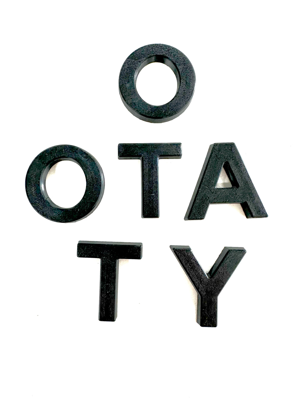 Black textured grille letters spelling "OTATY" arranged on a white background, part of the BPF 2024+ TRD PRO & Trailhunter Grille Letters set designed for truck customization.