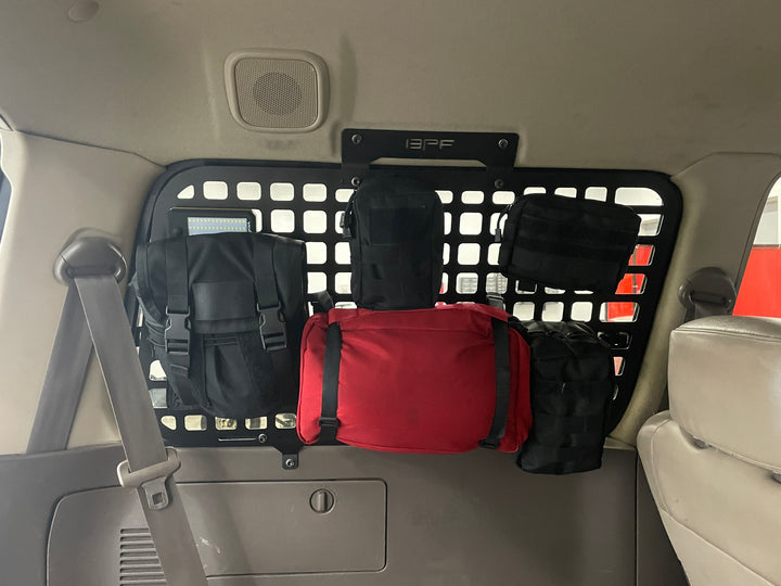 Interior view of a 1990-1997 Toyota Land Cruiser with BPF 1990-1997 Toyota Land Cruiser Storage Panels installed behind the rear seats, featuring multiple attached black and red MOLLE-compatible storage pouches for organized overlanding gear.