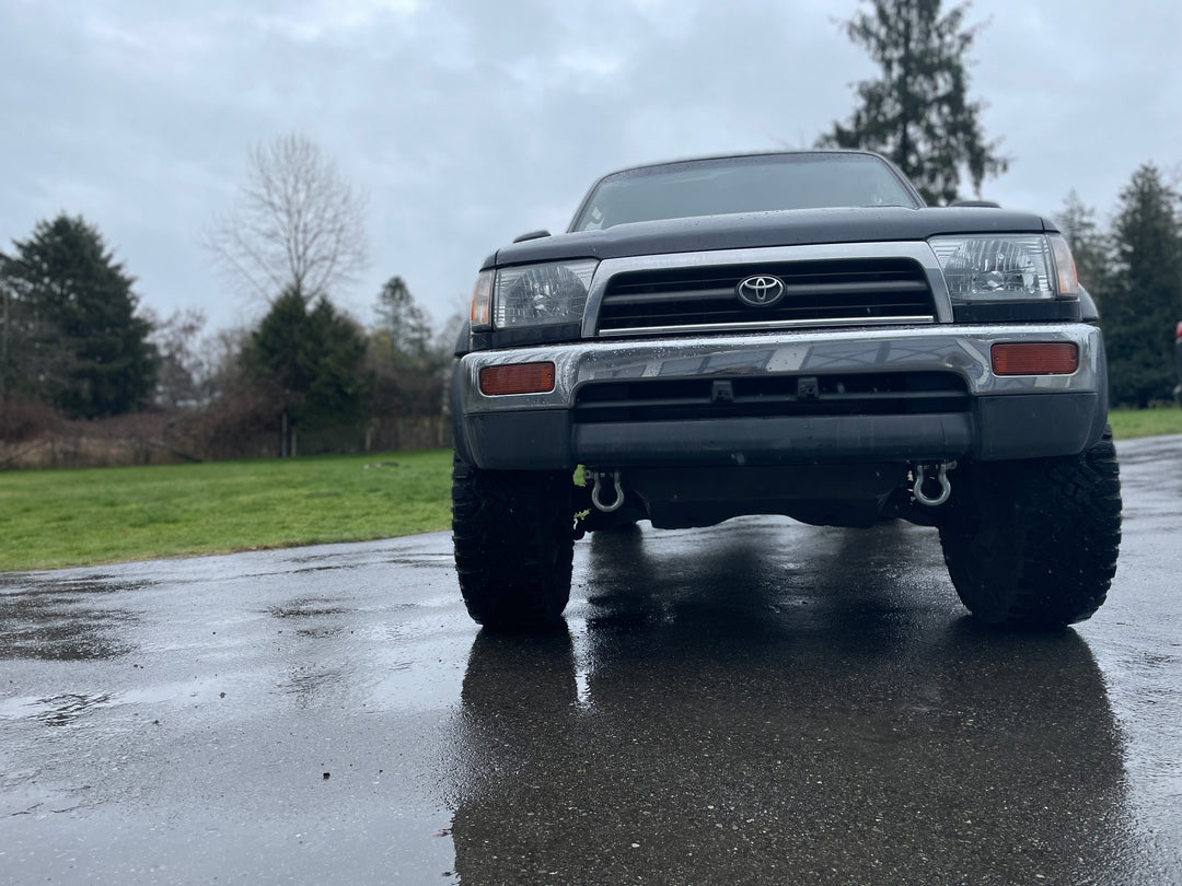 Front view of a Toyota 4Runner equipped with BPF 3rd gen 4Runner Tow Hook Set 1996-2002 mounted on the bumper in a wet outdoor setting.