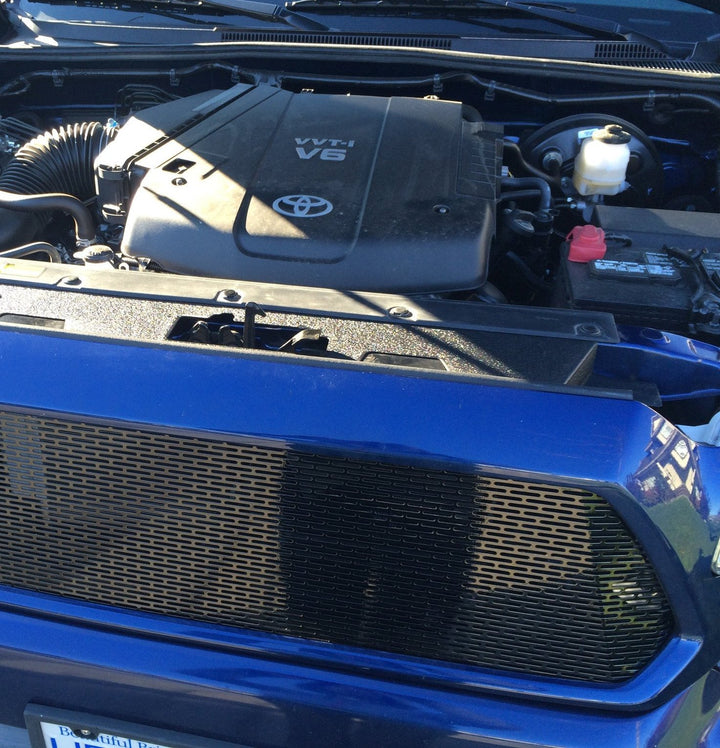 Close-up of a blue truck front grille featuring the BPF 12-15 Toyota Tacoma Cooling Panel installed, showcasing a durable black mesh design for improved airflow and engine cooling.