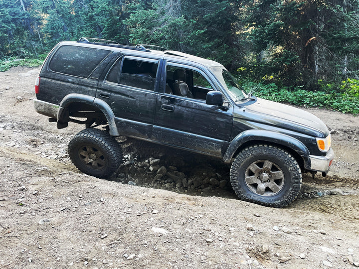 Black Toyota 4Runner navigating rough off-road terrain, equipped with BPF 1996-2002 Toyota 4Runner Light Brackets for enhanced durability and secure light mounting.